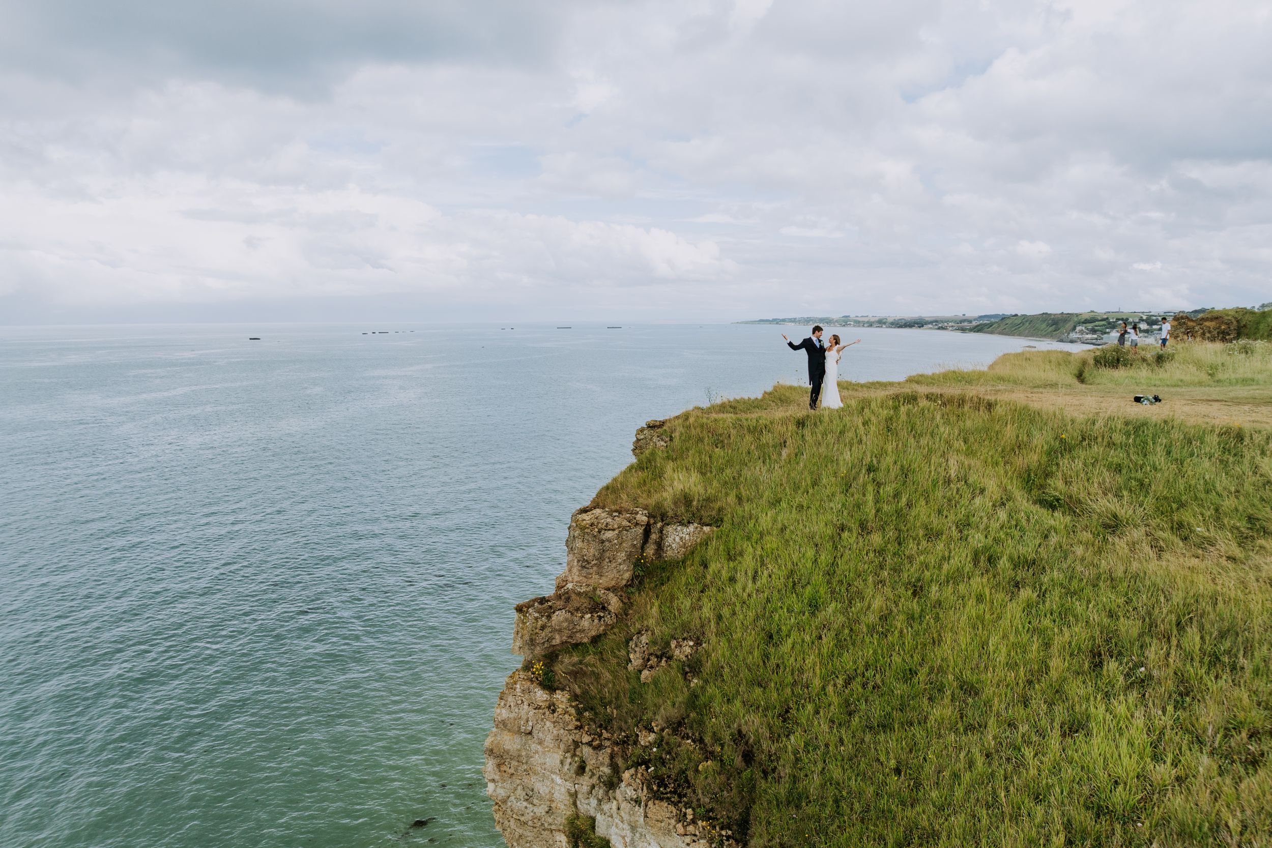 Les mariés, tout petits au bord d'une falaise verte qui tombe dans la mer, vus du ciel