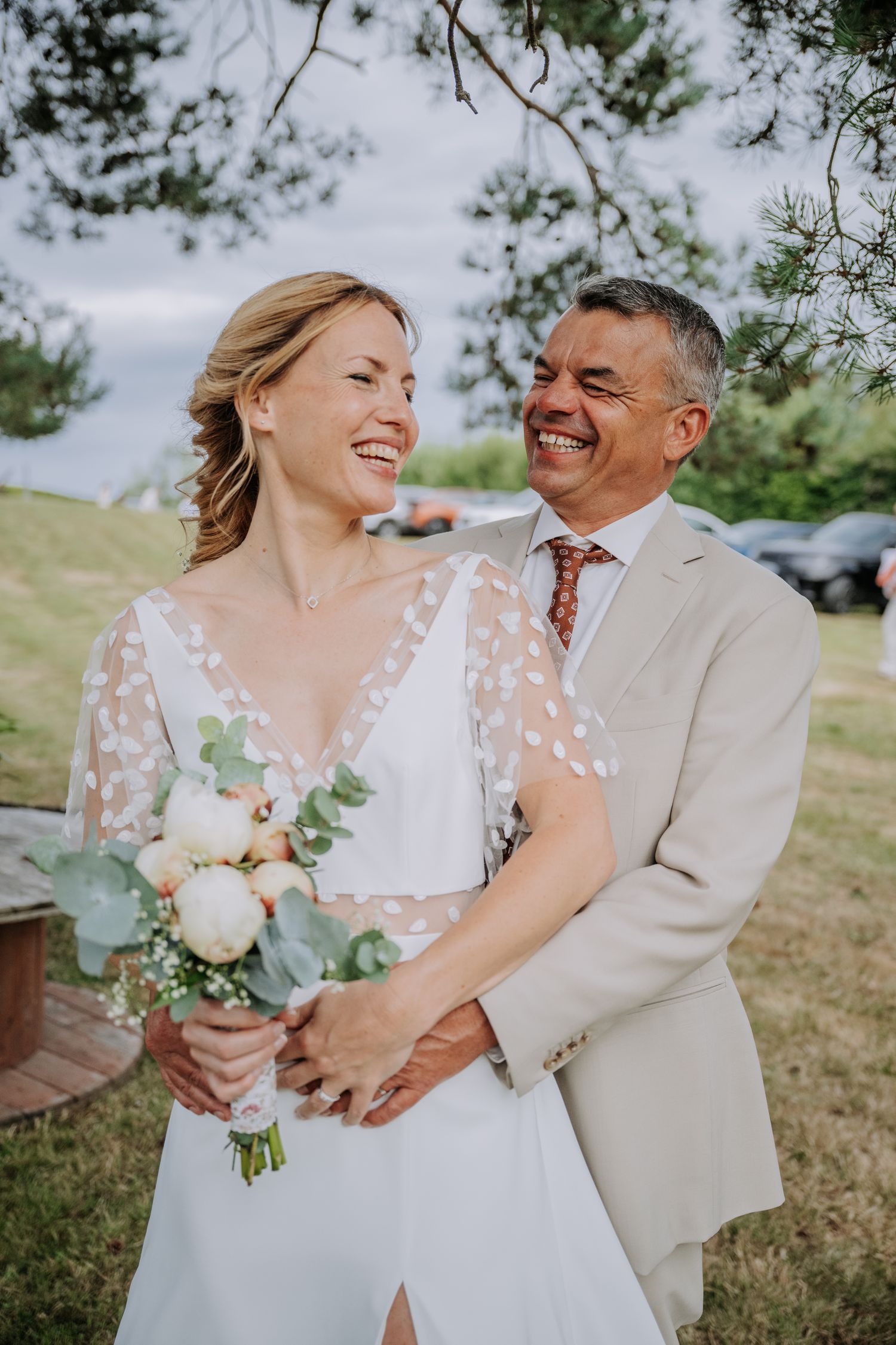 Emmanuelle rit aux éclats dans les bras de David, bouquet de pivoines à la main