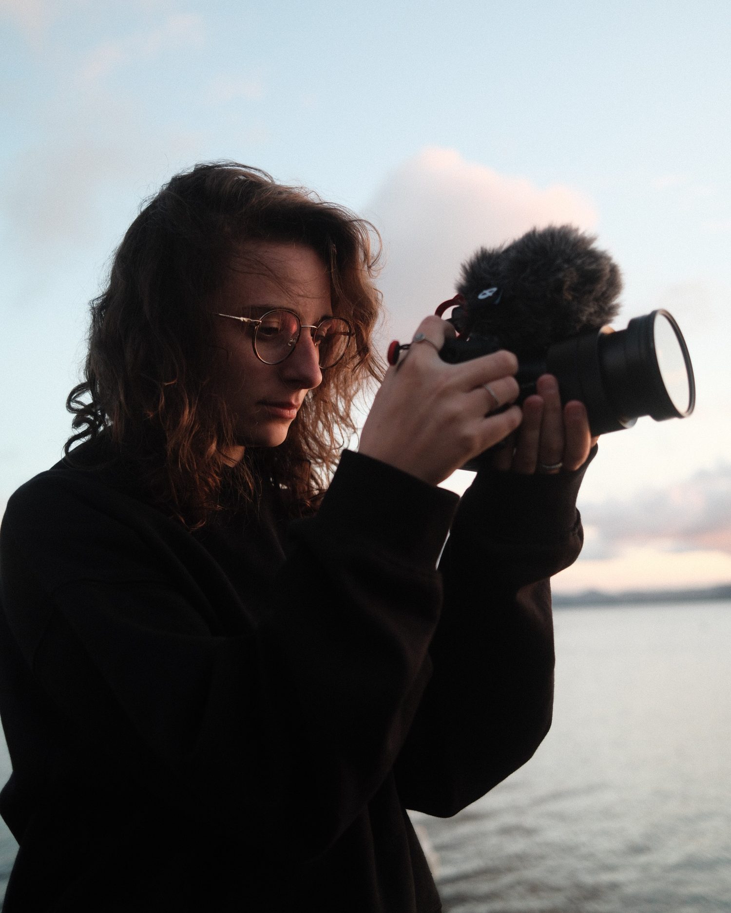 Alexandra, caméra en main, face à la mer au coucher du soleil