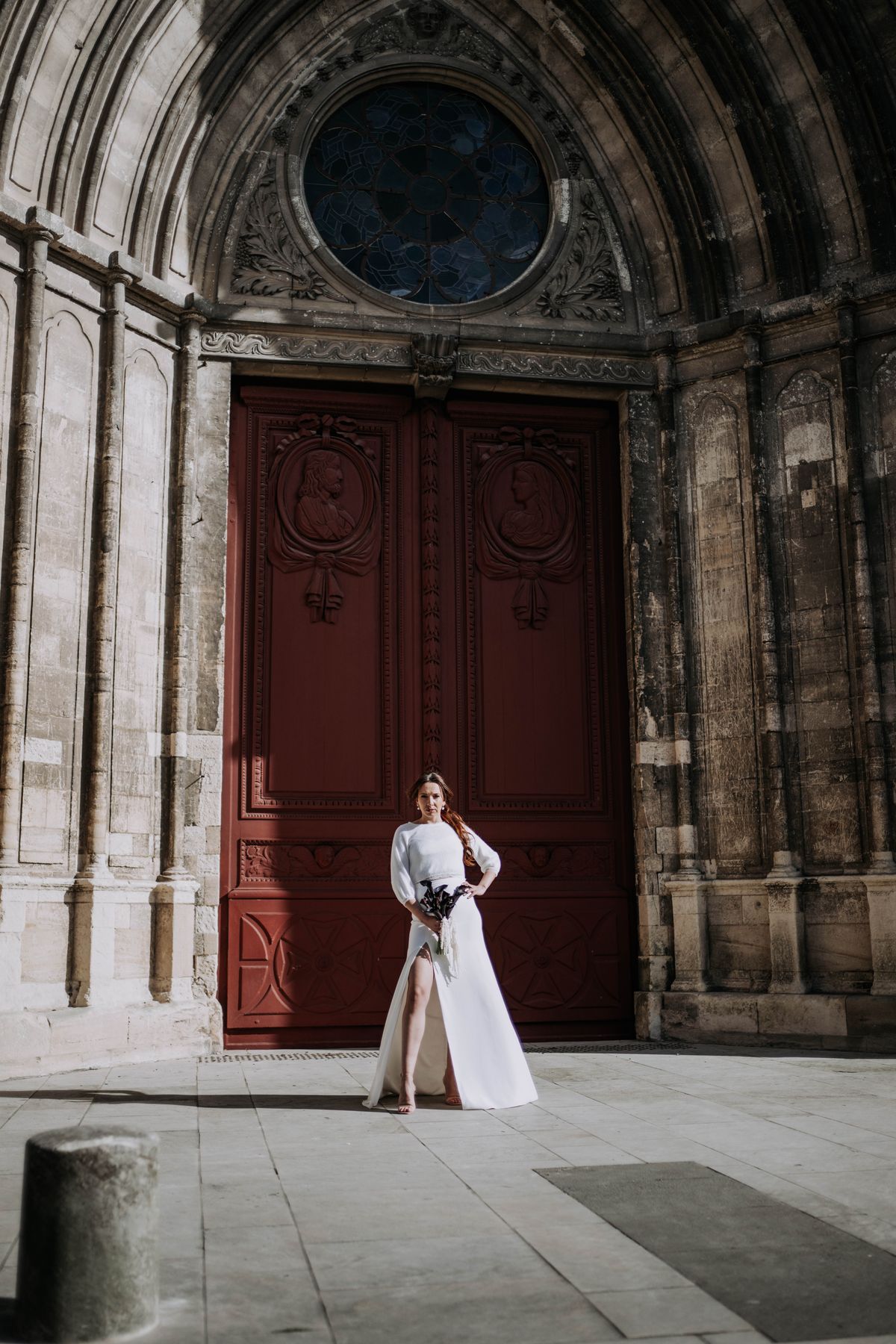 Une mariée devant la grande porte rouge d'une cathédrale, lors d'une séance inspiration à Bayeux