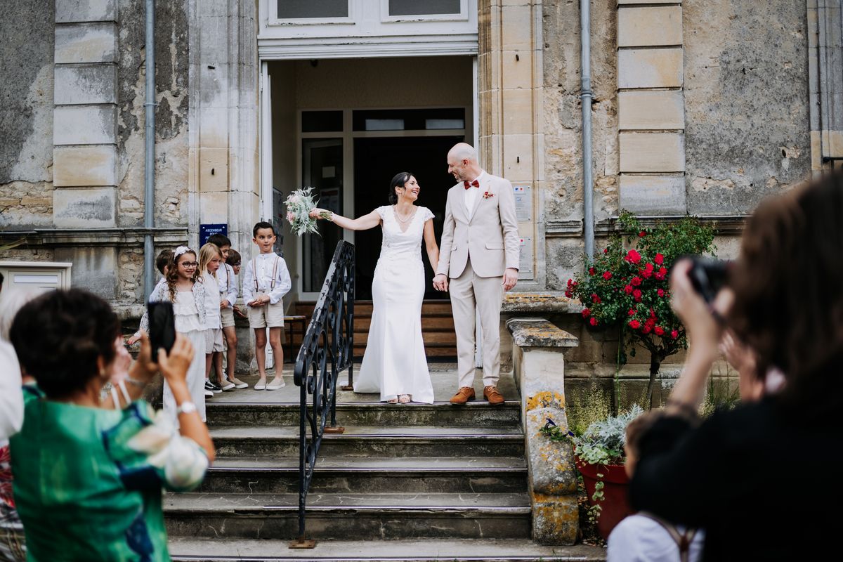 Teresa et Julien descendent le perron d'une demeure en pierre, accueillis par leurs invités